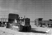 Un trattore dell'esercito con rimorchio e un camion si incrociano lungo una pista nel deserto.jpg