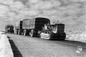 Un trattore traina due grandi rimorchi lungo una strada nel deserto seguito da un camion.jpg